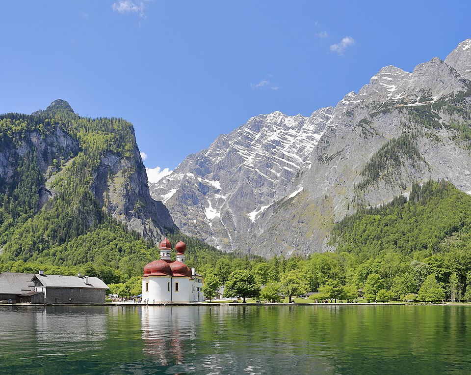 The red-domed church of St. Bartholomä on a green peninsula of the Königssee, with the rock walls of the Watzmann rising behind.