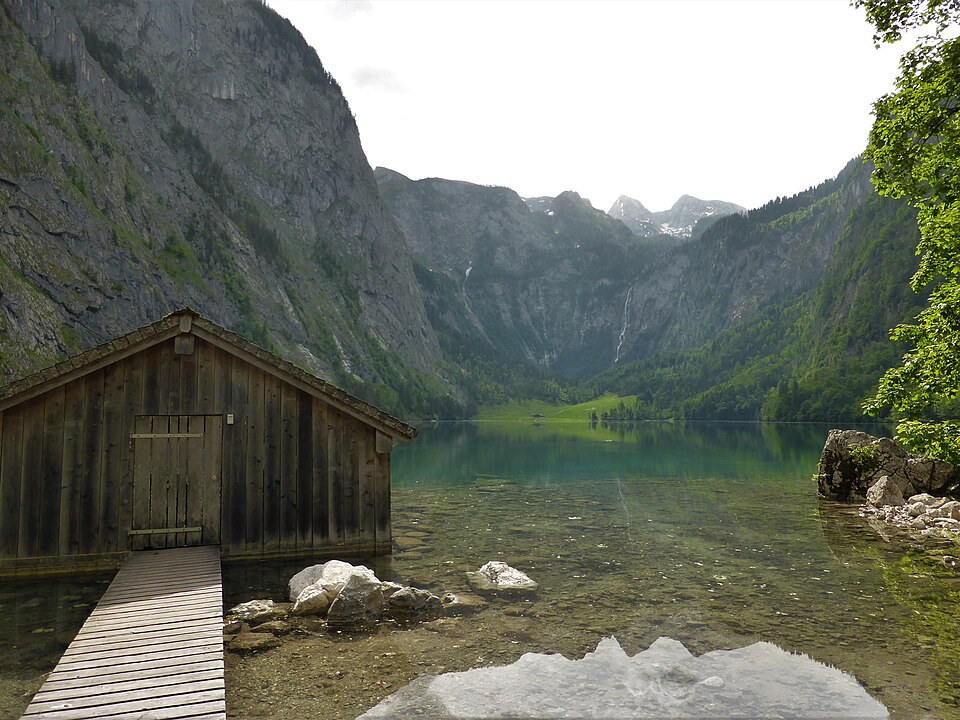 A weathered wooden boathouse on the clear Obersee with steep rock walls of the national park enclosing the lake.